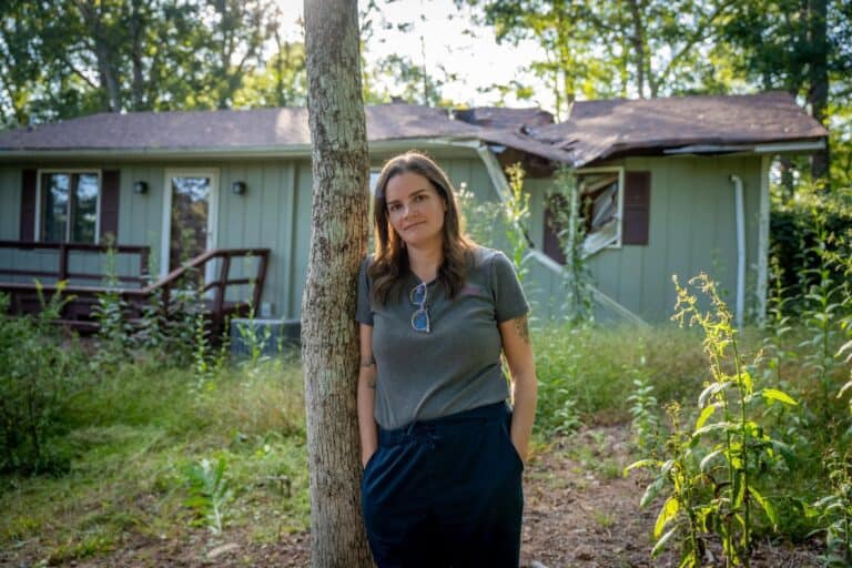 Hannah stands outside her damaged home a year after Hurricane Helene sent an oak tree crashing through the roof. Photo/Americares.